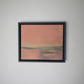 A framed abstract landscape painting featuring a soft pink and peach sky over muted green and gray land, housed in a dark charcoal frame and mounted on a plain white wall.